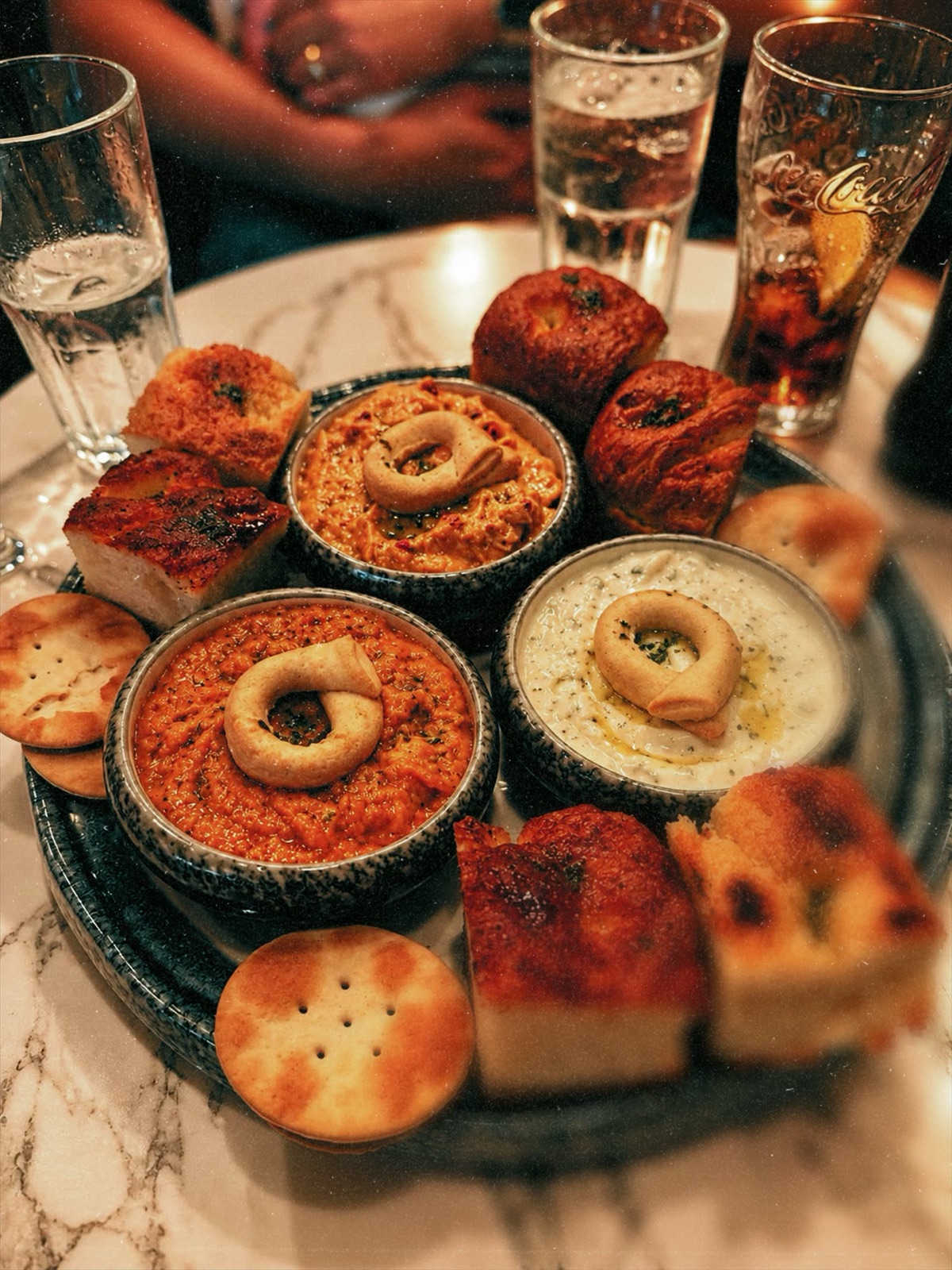 A sharing platter of three dips with focaccia and crackers, drinks on the table