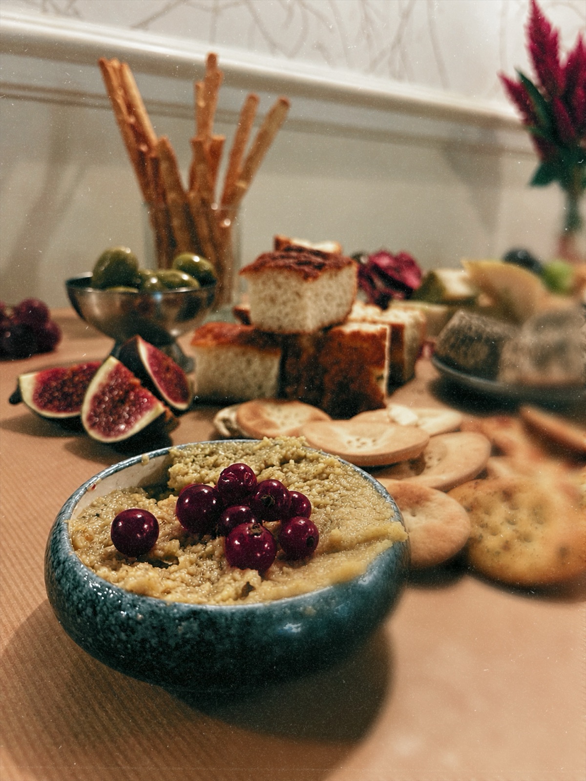 A dip topped with cherries beside fresh figs, grissini and focaccia on a grazing table