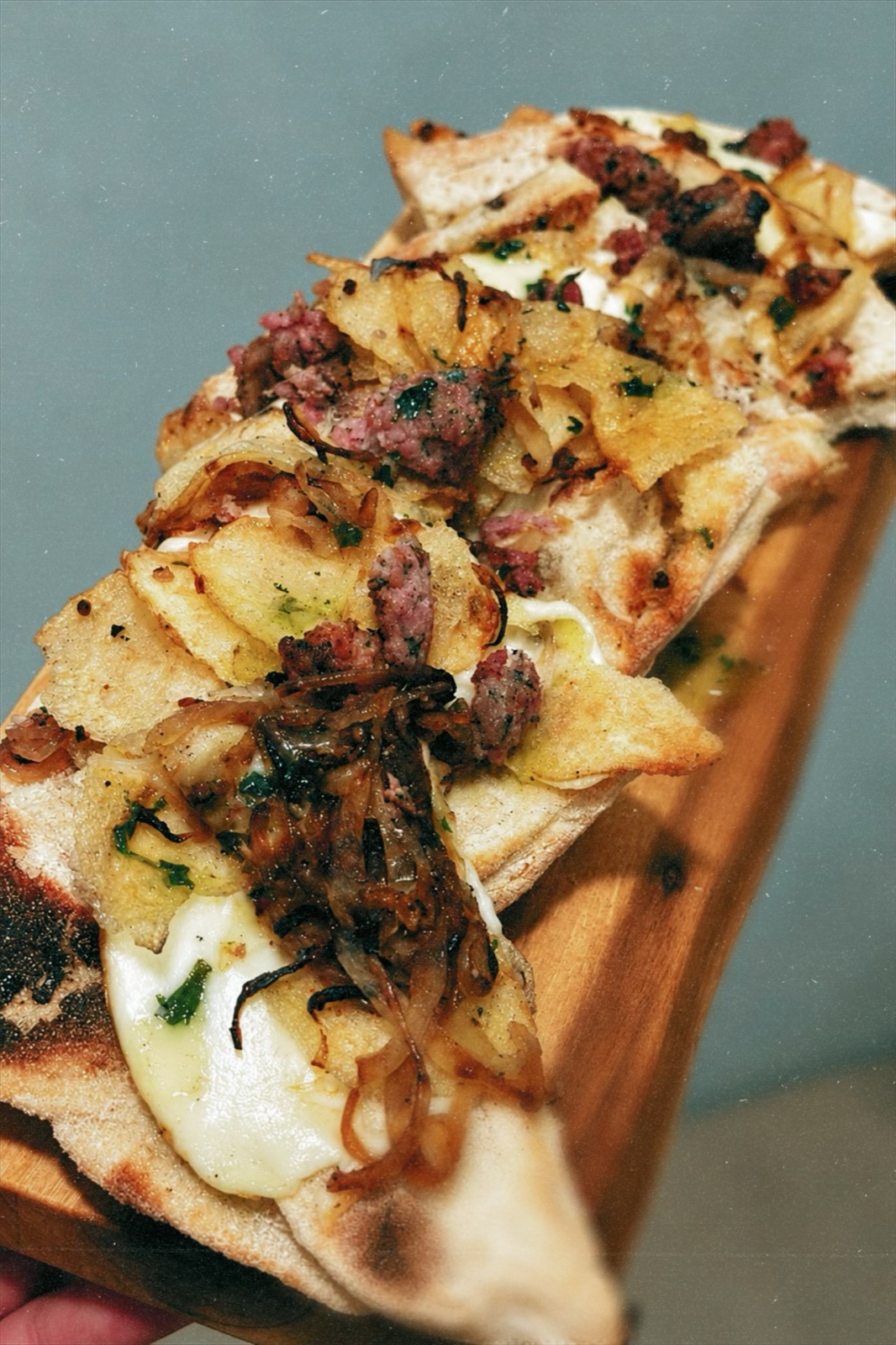 A pinsa with sausage, caramelised onions and melted cheese on a wooden board